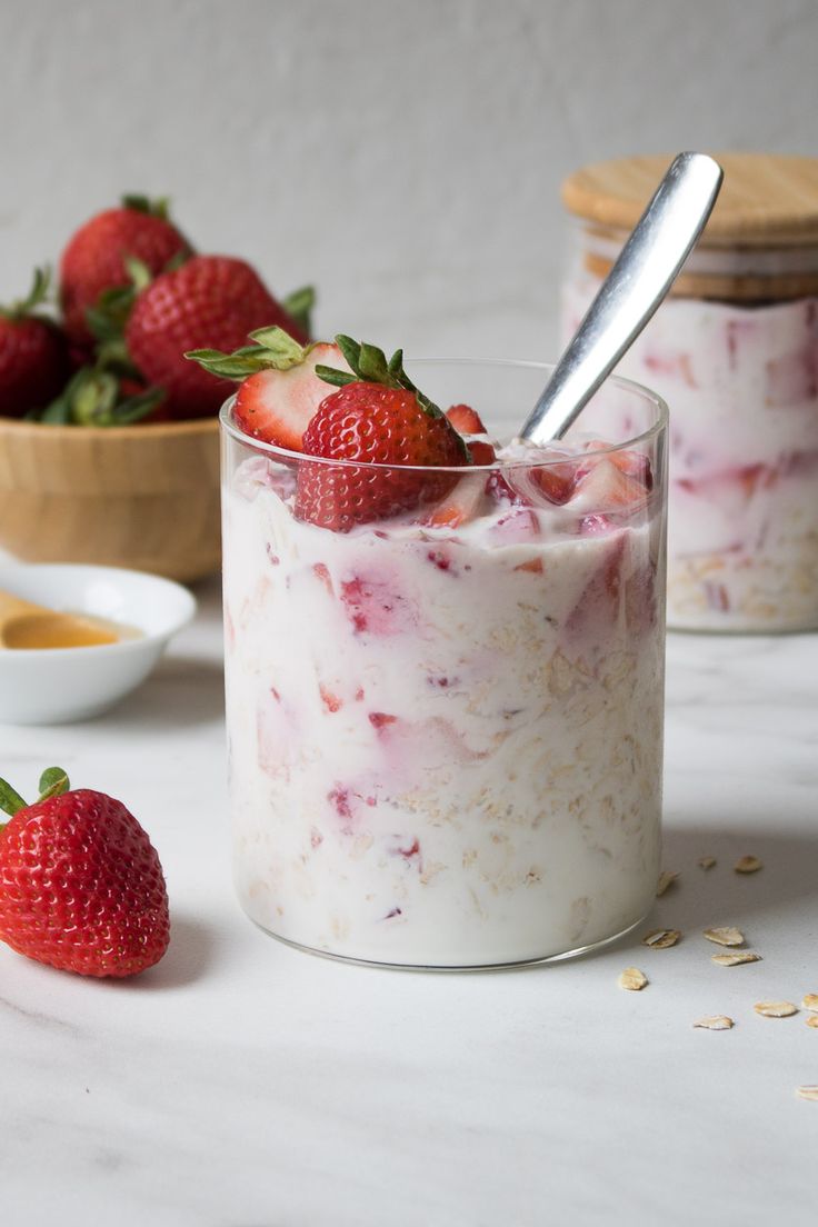 two jars filled with yogurt, strawberries and oatmeal on a table