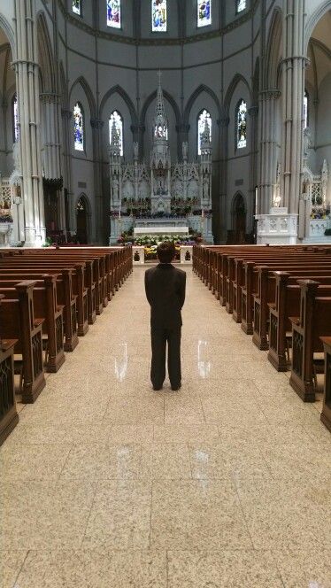 a man standing in the middle of a church looking at pews and stained glass windows