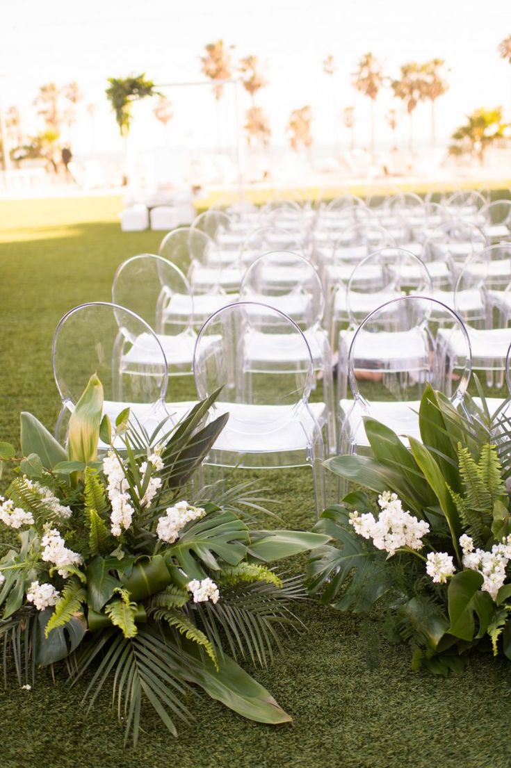 an outdoor ceremony setup with chairs and flowers on the grass in front of palm trees