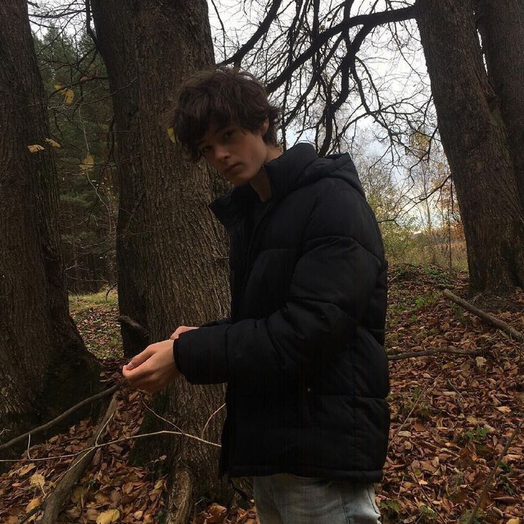 a young man standing next to a tree in the woods