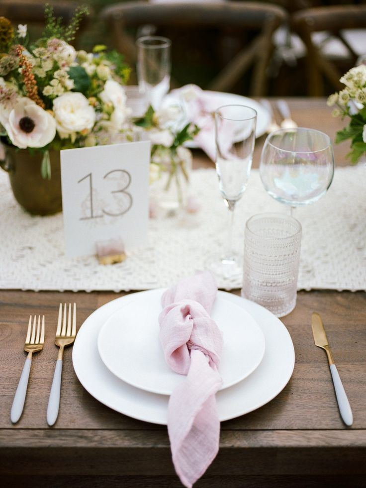 the table is set with white plates, silverware and pink napkins on it