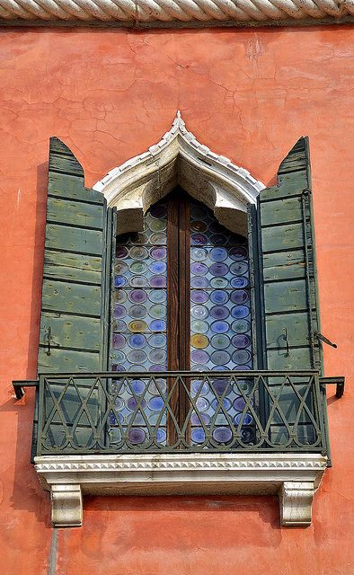 an open window on the side of a building with green shutters and ornate iron work