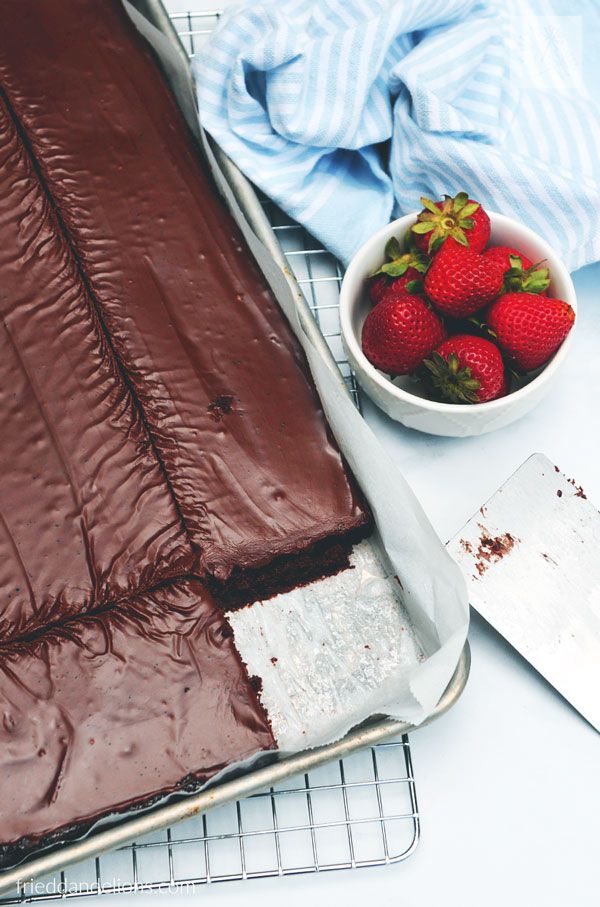 a chocolate cake with strawberries in a bowl next to it on a cooling rack