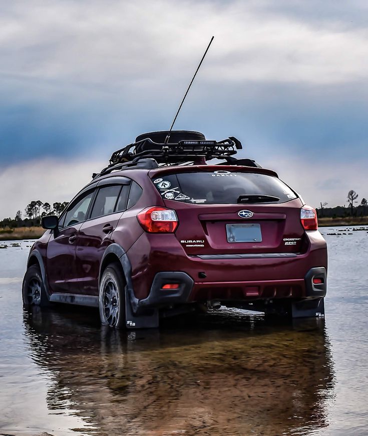 the back end of a red subarunt parked in shallow water on a cloudy day