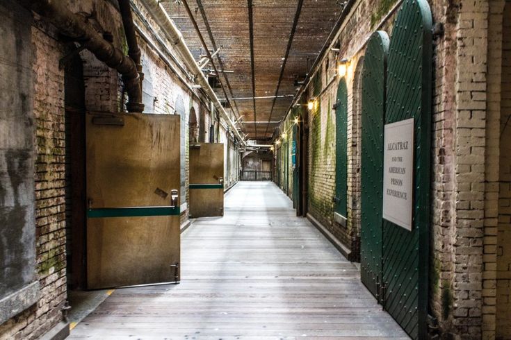 an empty hallway with green doors leading to another room that has brick walls and wooden floors