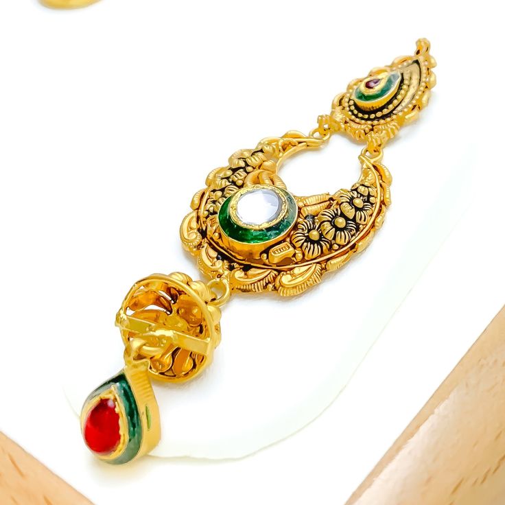 This magnificent choker set, crafted from 22k gold with an antique finish, weighs 69.1 grams. It showcases opulent paisley motifs accented with Kundan stones. The necklace is 14.5 inches long and 1.5 inches wide, featuring a drop length of 0.9 inches, creating a statement of refined elegance. With 1 inch of adjustable links, it ensures a perfect fit, secured by a hook lock. The set includes matching earrings, each 3 inches in length, equipped with screw-back posts for secure wear. This ensemble 22k Gold Tikka With Intricate Design, Diwali 22k Gold Tikka With Intricate Design, Traditional 22k Gold Tikka, Gold Tikka With Intricate Design As Gift, Gold Tikka With Intricate Design For Gift, Ceremonial 22k Gold Tikka With Intricate Design, Ornate Gold Kundan Chandbalis, Ornate Gold Chandbalis With Kundan, 22k Gold Tikka With Intricate Design For Festive Occasions