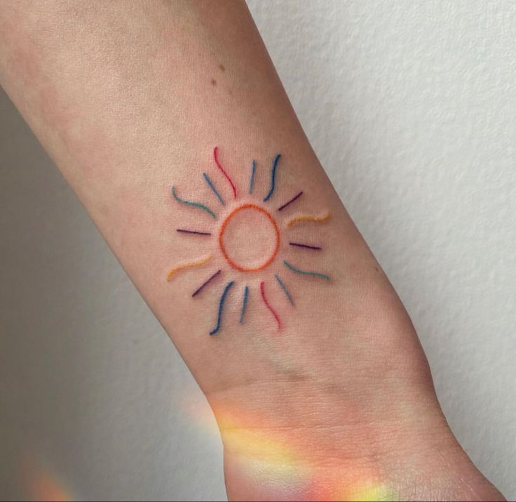 a small sun tattoo on the wrist with colored crayons all over it's arm