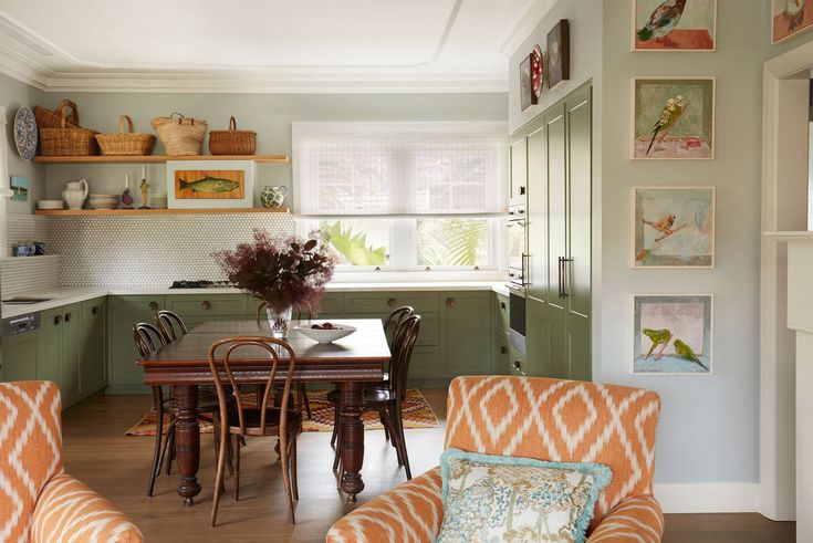 a kitchen with green cabinets and orange chairs in front of a dining room table surrounded by pictures on the wall