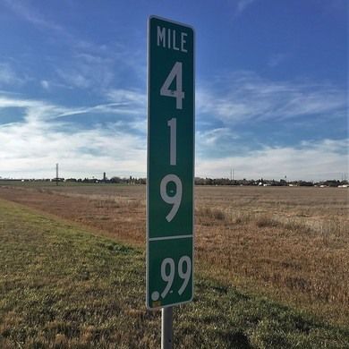 a road sign on the side of a dirt road in an open field with grass