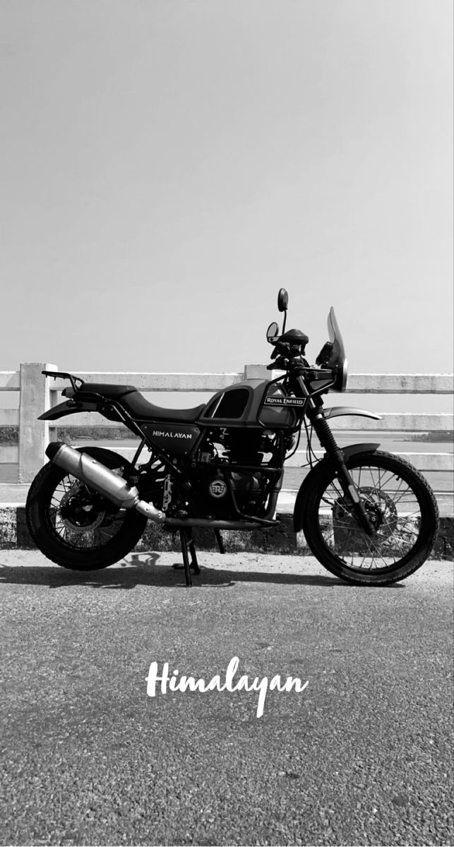 a black and white photo of a motorcycle parked in front of a wooden fence with the words himalayan on it