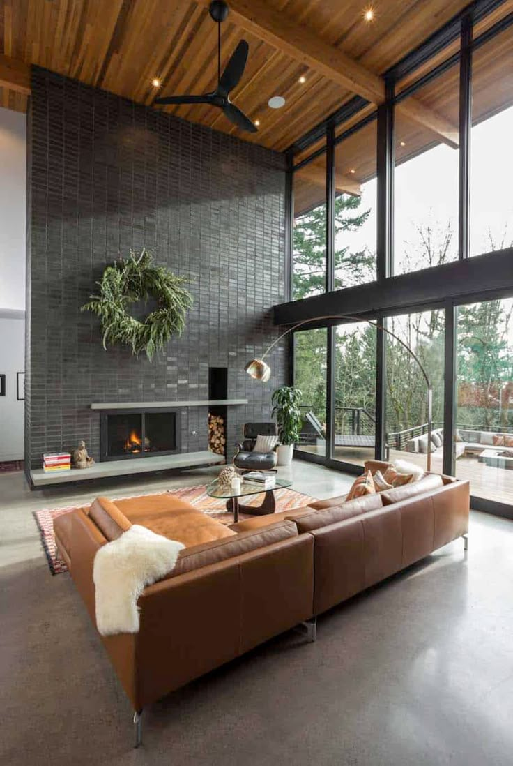 a living room with couches and a fireplace in the center, surrounded by large windows