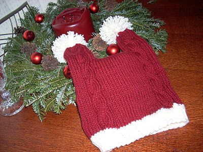 a red knitted hat with white pom - poms sits on a table next to christmas decorations