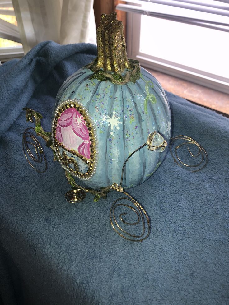 a decorative blue pumpkin sitting on top of a blue cloth covered table next to a window