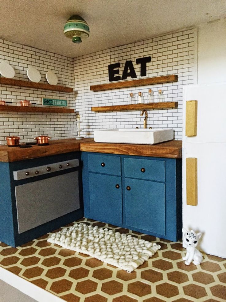 a toy kitchen with blue cabinets and white brick wall behind the stovetop, sink and dishwasher