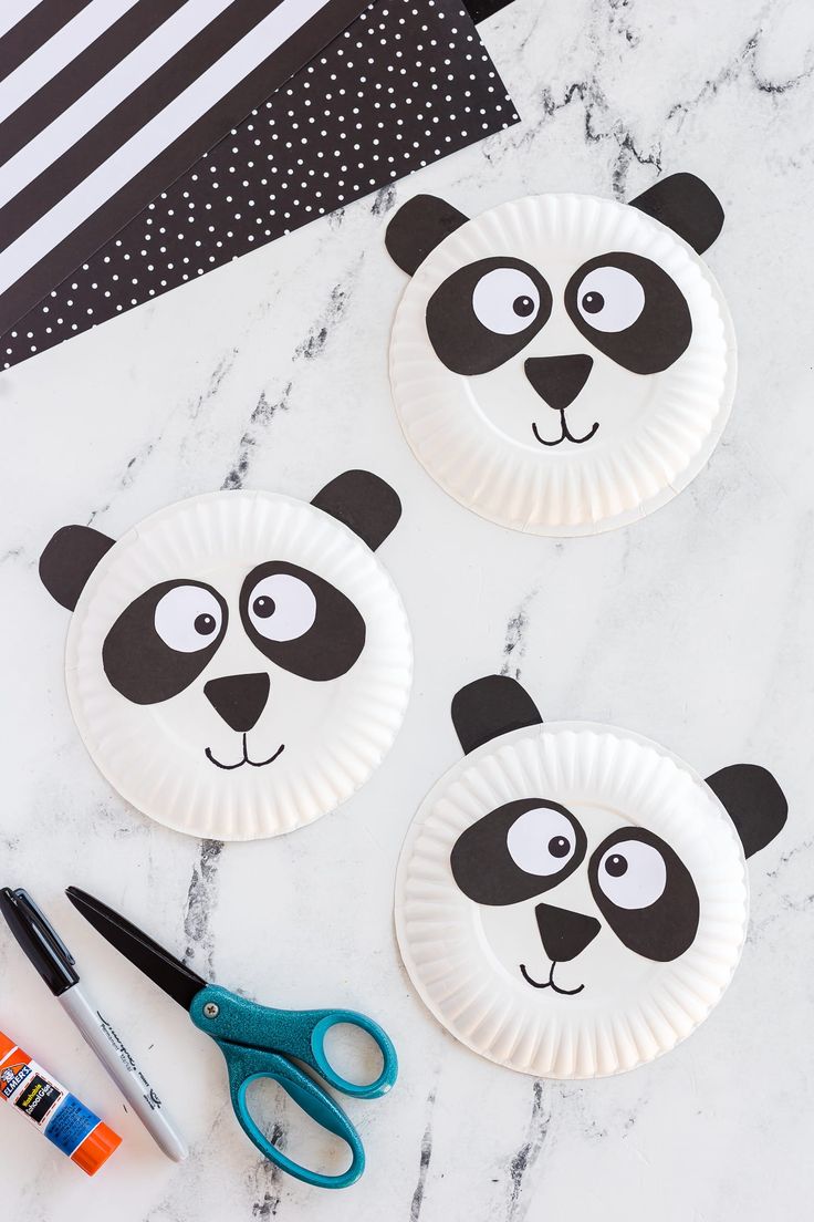 three paper plates with panda faces and scissors on a marble countertop next to markers