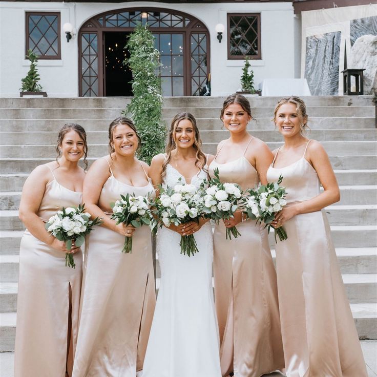 a group of women standing next to each other in front of a building holding bouquets