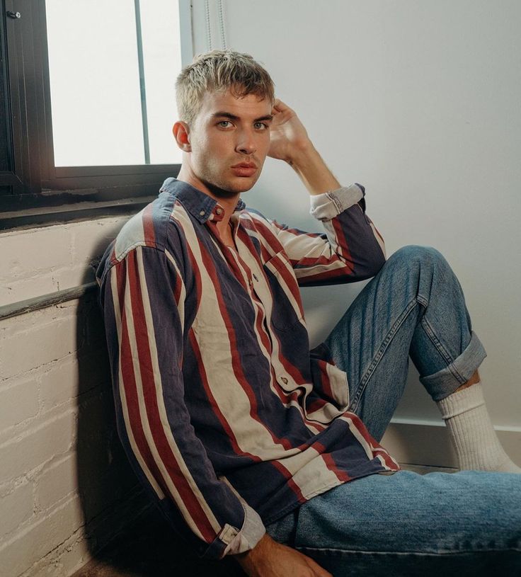 a young man sitting on the floor with his hands in his hair and looking at the camera