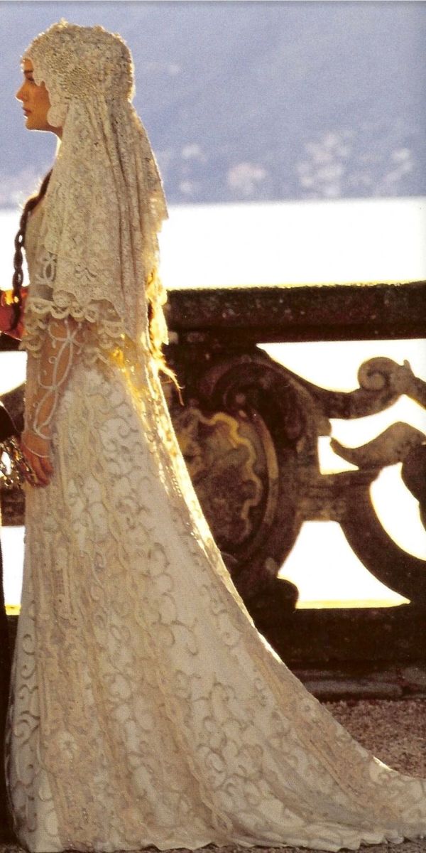 a bride and groom standing next to each other in front of a fence with mountains behind them