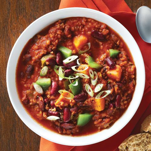 a bowl of chili with beans, avocado and bread on a red napkin