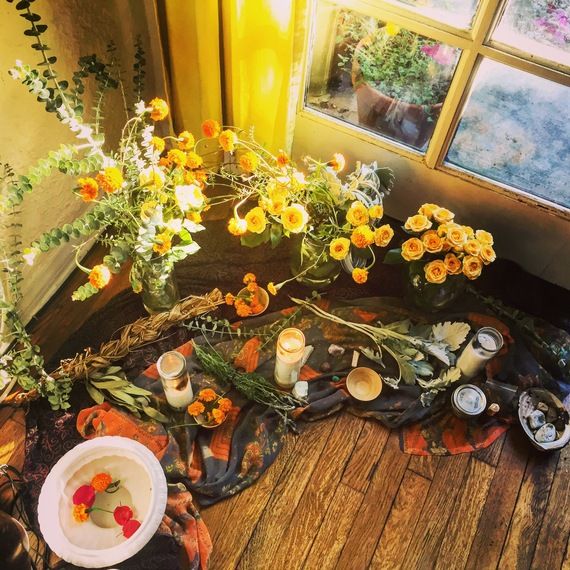 flowers and candles sit on the floor next to an open window with yellow pansies