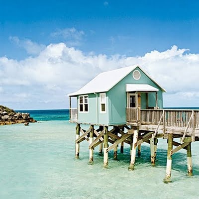 a small blue house sitting on top of a wooden pier next to the ocean with clear water