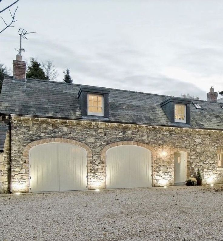 a large stone house with three garages and lights on the side of it's windows