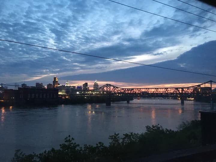 the sun is setting over a river with power lines in the foreground and a bridge on the other side