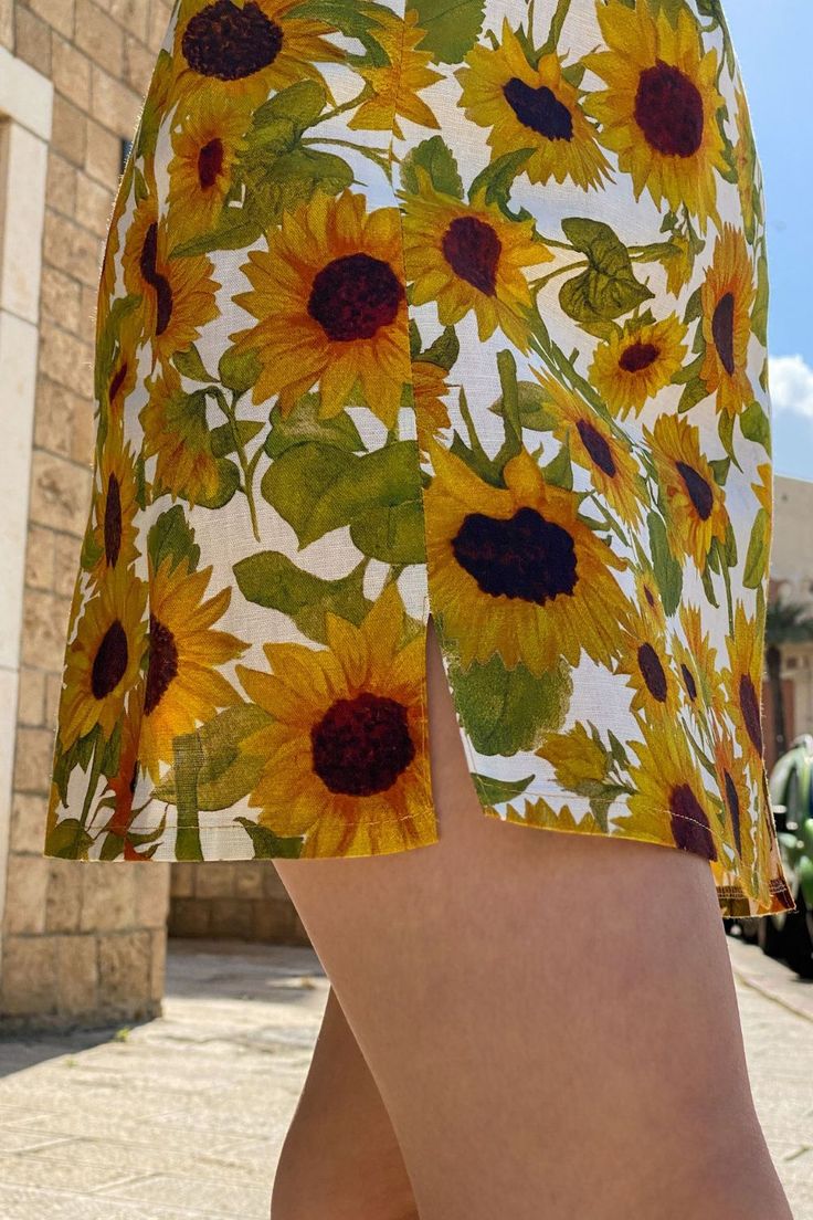 Your next favorite statement piece. Two subtle slits at the front add light detail to the summer mini skirt. A hand painted sunflowers print adorn the skirt. With warm yellow shades emanating bright, cheerful vibes, it's hard not to love this little number. The beautifully hand-painted sunflower print makes this a confidence-boosting style. The Rachel Skirt in Sunees creates a summery, colorful outfit full of vibrant energy. The floral mini skirt is made from 100% linen Fitted Linen Mini Skirt For Summer, Floral Print Beach Skirt For Spring, Fitted Printed Mini Skirt For Summer, Floral Print Mini Skirt For Summer Beach, Multicolor Printed Summer Skirt, Printed Summer Skirt For Day Out, Summer Day Out Printed Skirt, Floral Print Mini Skirt For Garden Party, Green Printed Summer Skirt