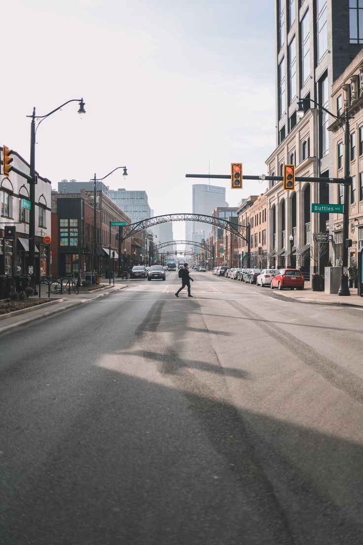 a person crossing the street in front of traffic lights and tall buildings on either side