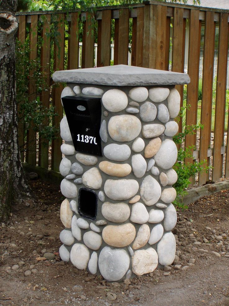 a stone mailbox sitting on the side of a road next to a wooden fence