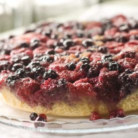 a pie with blueberries and other toppings is on a glass platter, ready to be eaten