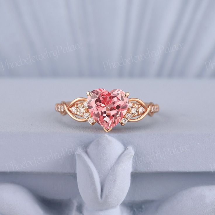 a pink heart shaped diamond ring on top of a white cloth