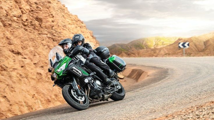 a man riding a motorcycle down a curvy road next to a rocky cliff