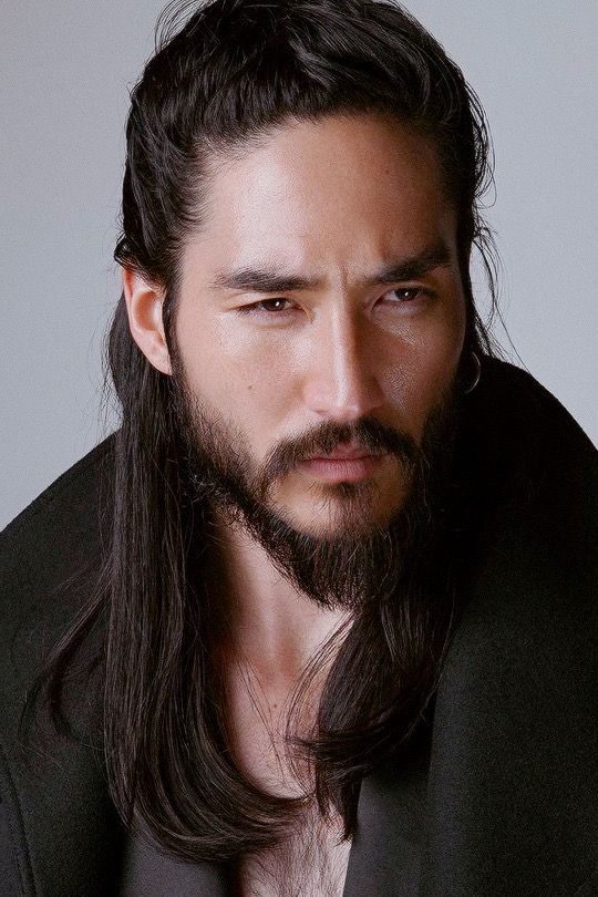 a man with long hair and a beard wearing a suit jacket looking at the camera