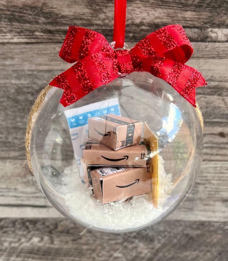 a glass ornament filled with boxes and a red ribbon