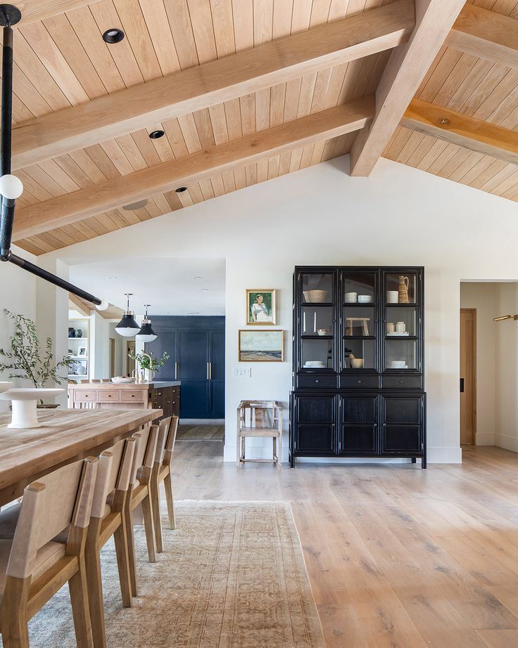 a dining room and kitchen area with wood flooring, white walls and ceiling beams