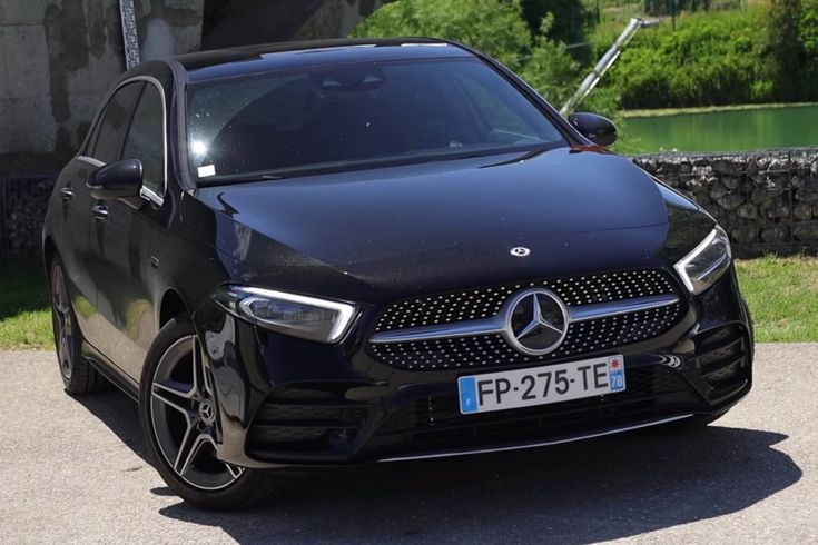 a black mercedes cla is parked in front of a stone wall and some water