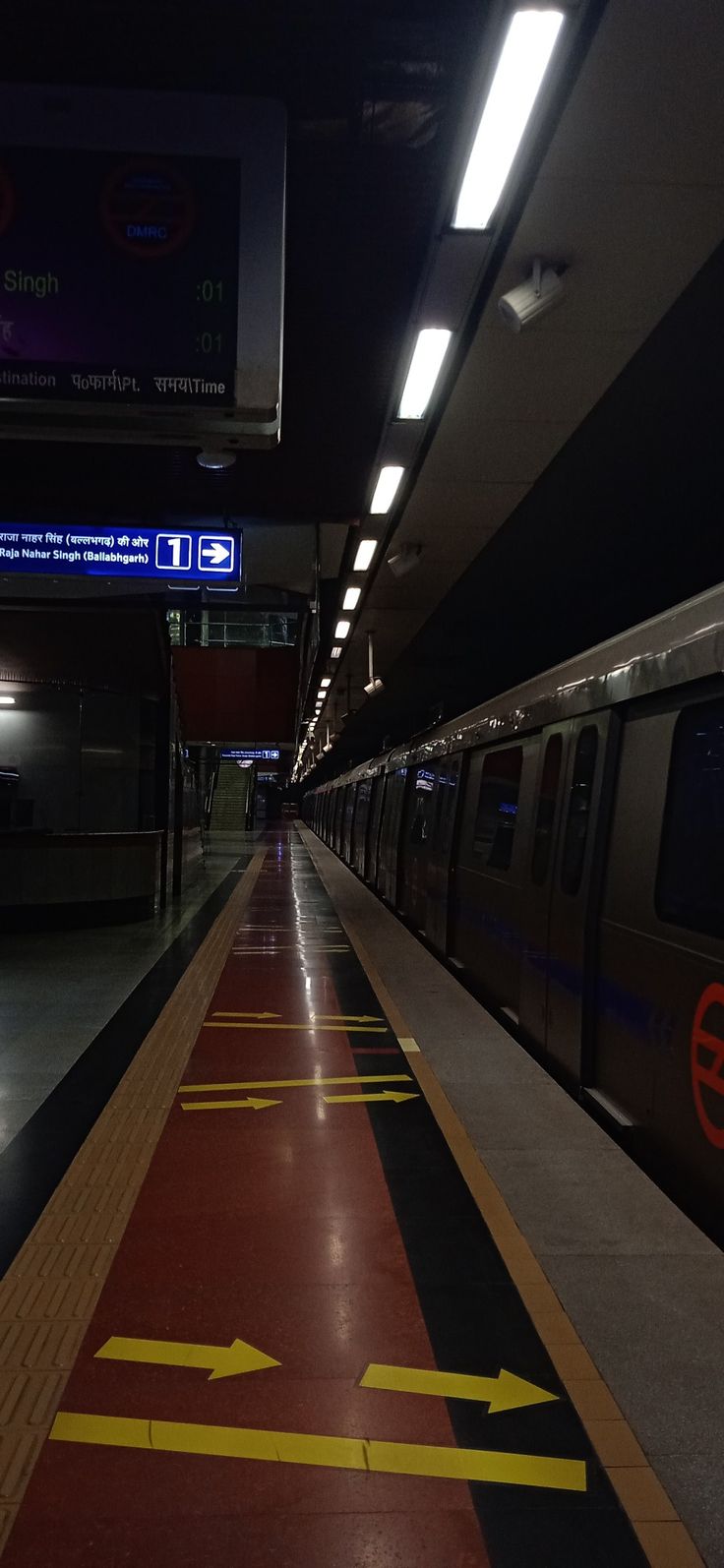 a subway train pulling into the station at night with its lights on and yellow arrows painted on the floor