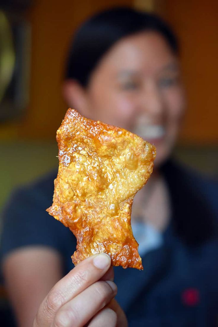 a person holding up a piece of food in front of their face and smiling at the camera