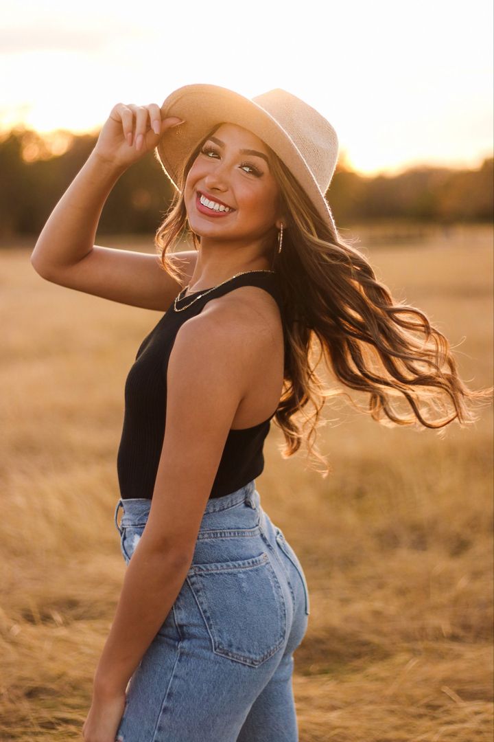 a beautiful young woman in jeans and a cowboy hat posing for a photo on an open field