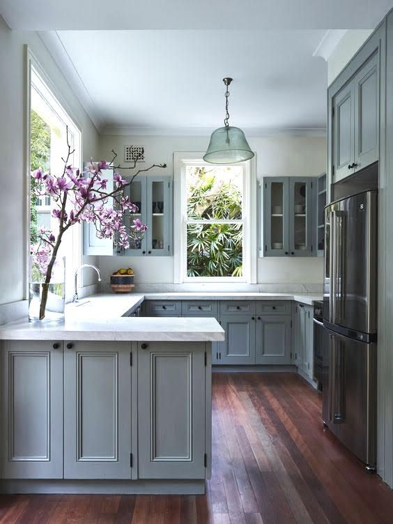 a kitchen with blue cabinets and white counter tops is pictured in this image, there are flowers on the window sill