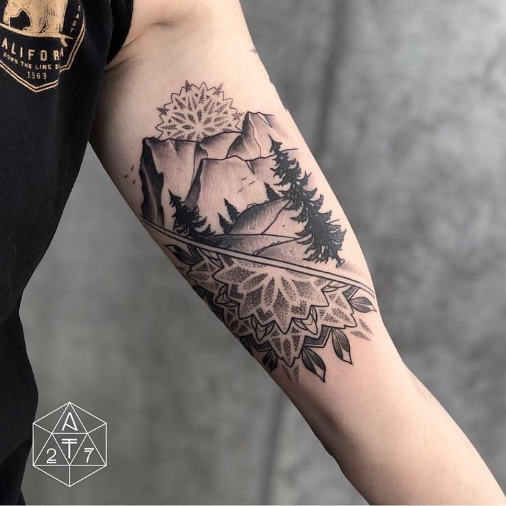 a man's arm with a mountain and pine tree tattoo on the left forearm