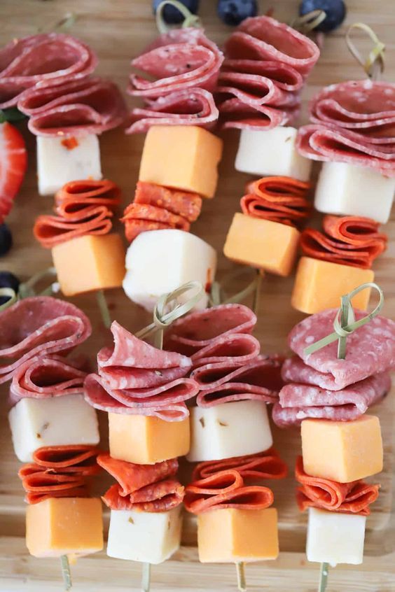 an assortment of appetizers are arranged on a cutting board with cheese, ham and blueberries