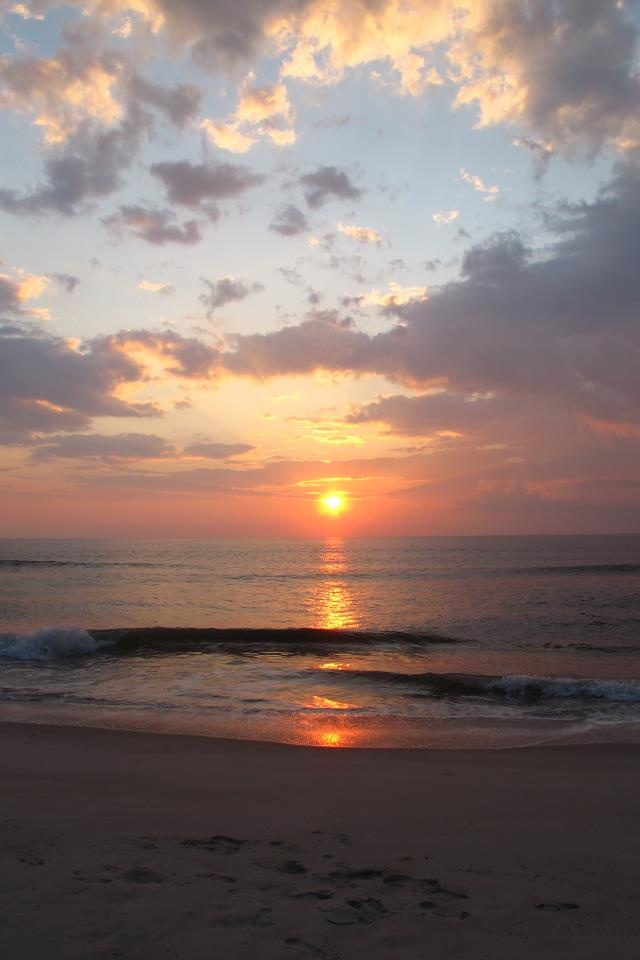 the sun is setting over the ocean with clouds in the sky and waves crashing on the beach