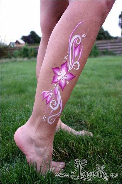 a woman's legs with pink flowers painted on the side of her leg, in grass