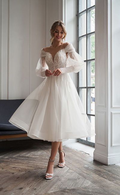 a woman wearing a white wedding dress standing in front of a window with her hands on her hips