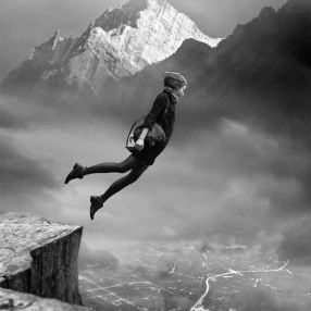 a person jumping in the air on top of a mountain with snow capped mountains behind them