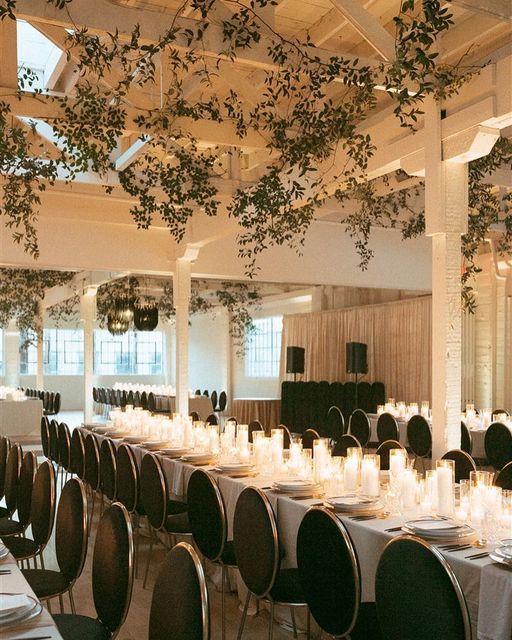 the tables are set up for an event with candles and greenery hanging from the ceiling