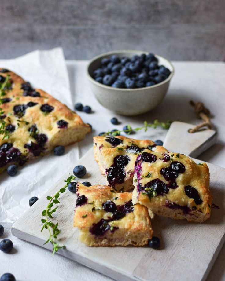 blueberry scones on a cutting board next to a bowl of blueberries