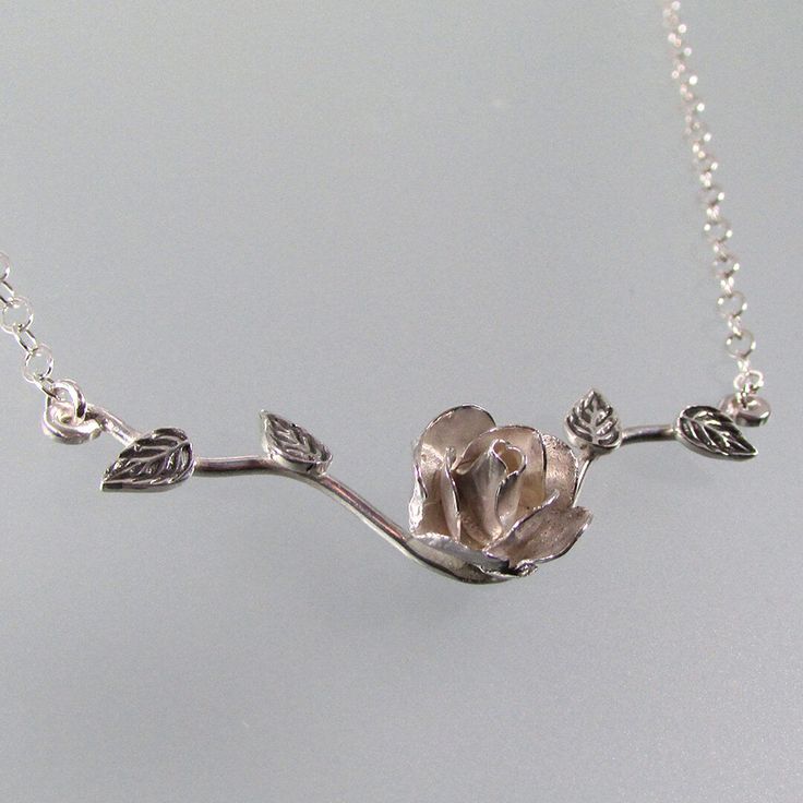 ***Temporarily Sold Out - New Design Coming Soon*** Adorn your neck with an elegant rose that will never fade in this sterling silver rose necklace. Hand-wrought from recycled sterling silver, each rose petal is hand-sculpted and textured to form the delicate rose flower which is set upon a slim leaf-adorned branch that suspends from your choice of an 18 or 20 inch sterling silver cable chain. Roses commonly symbolize love and affection, but a rose’s color can also determine its meaning. Click h Elegant Rose Flower Necklace With Rose Design, Sterling Silver Rose Gold Jewelry With Rose Design, Elegant Sterling Silver Jewelry With Rose Design, Elegant Rose Sterling Silver Necklace, Elegant Silver Necklace With Rose Design, Elegant Rose Flower Pendant Necklace, Sterling Silver Necklace With Rose Flower Pendant, Silver Flower Pendant Jewelry With Rose Design, Silver Dainty Necklace With Rose Design